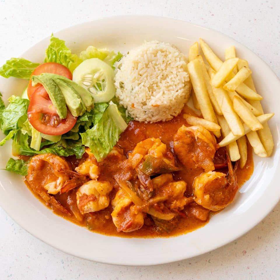 Plate of shrimp in tomato sauce with rice, French fries, and a fresh lettuce, tomato, cucumber, and avocado salad.